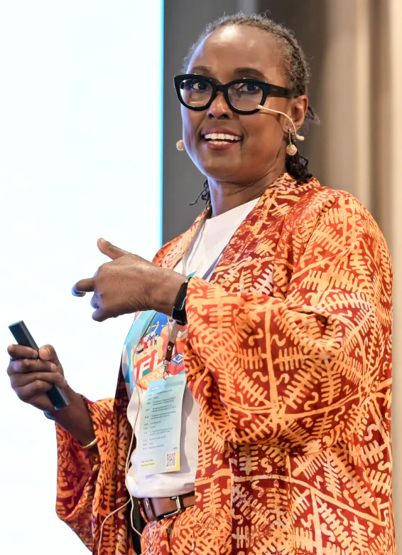 Dr. Égo Obi speaking on stage with a presentation clicker, gesturing to the audience
